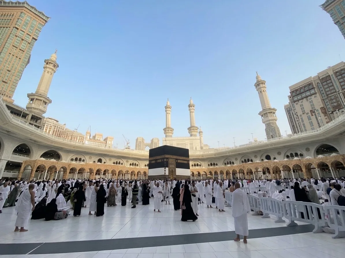 La Kaaba au centre de la Mosquée sacrée, entourée de pèlerins en ihram, sous un ciel bleu.
